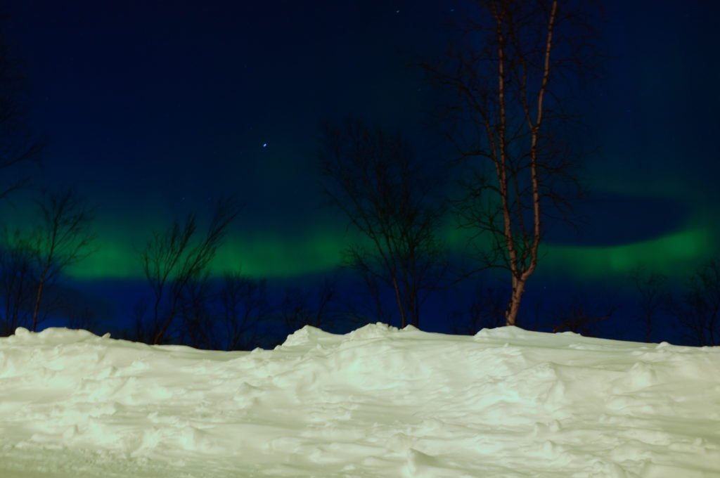 A slight view of some small band of the Northern lights in Abisko, Sweden, seen low on the horizon over the snow.
