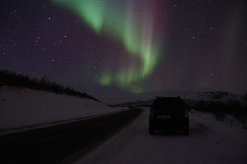 A car pulled over on the side of a road in Abisko, Sweden, to admire the Northern lights overhead