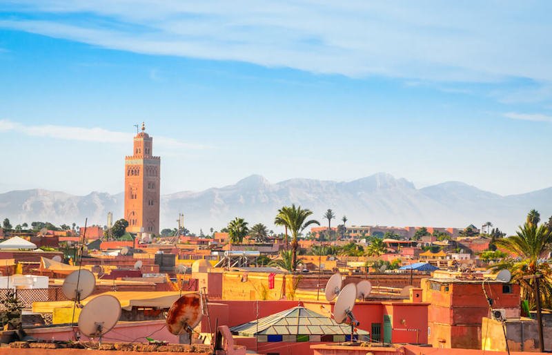 The rooftops of Marrakech with the tall minaret of the mosque and Atlas Mountains in the distance on a sunny day