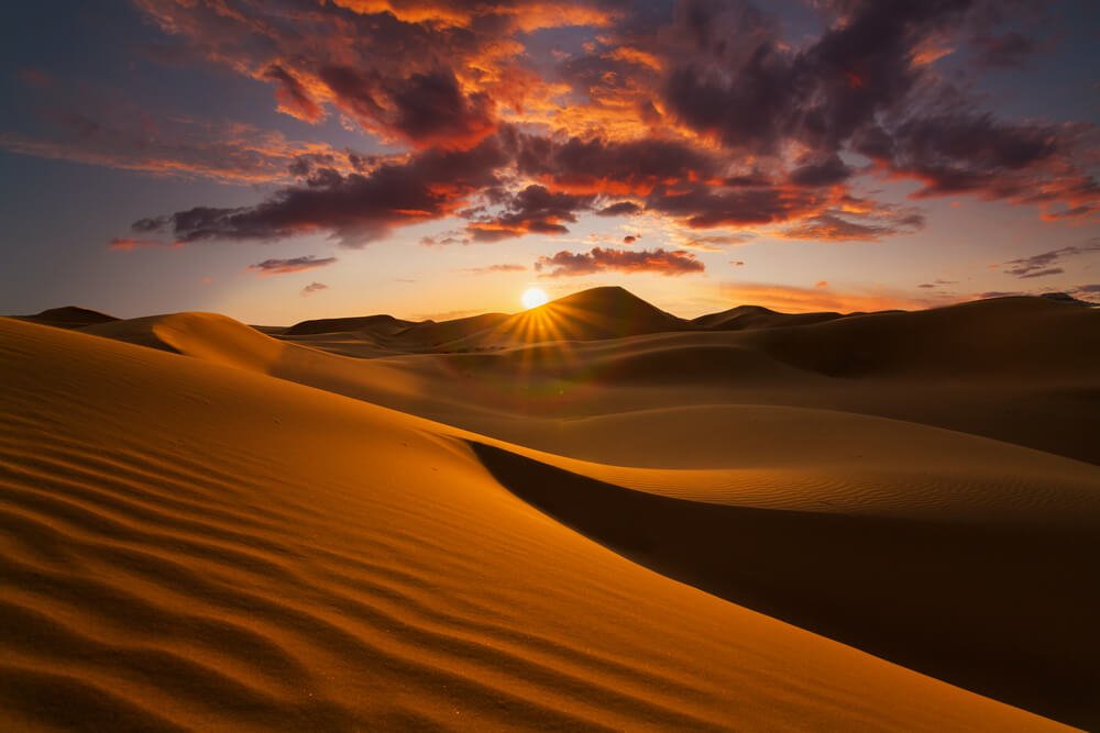 The sun setting over the Sahara Desert with brilliant pink and dark clouds