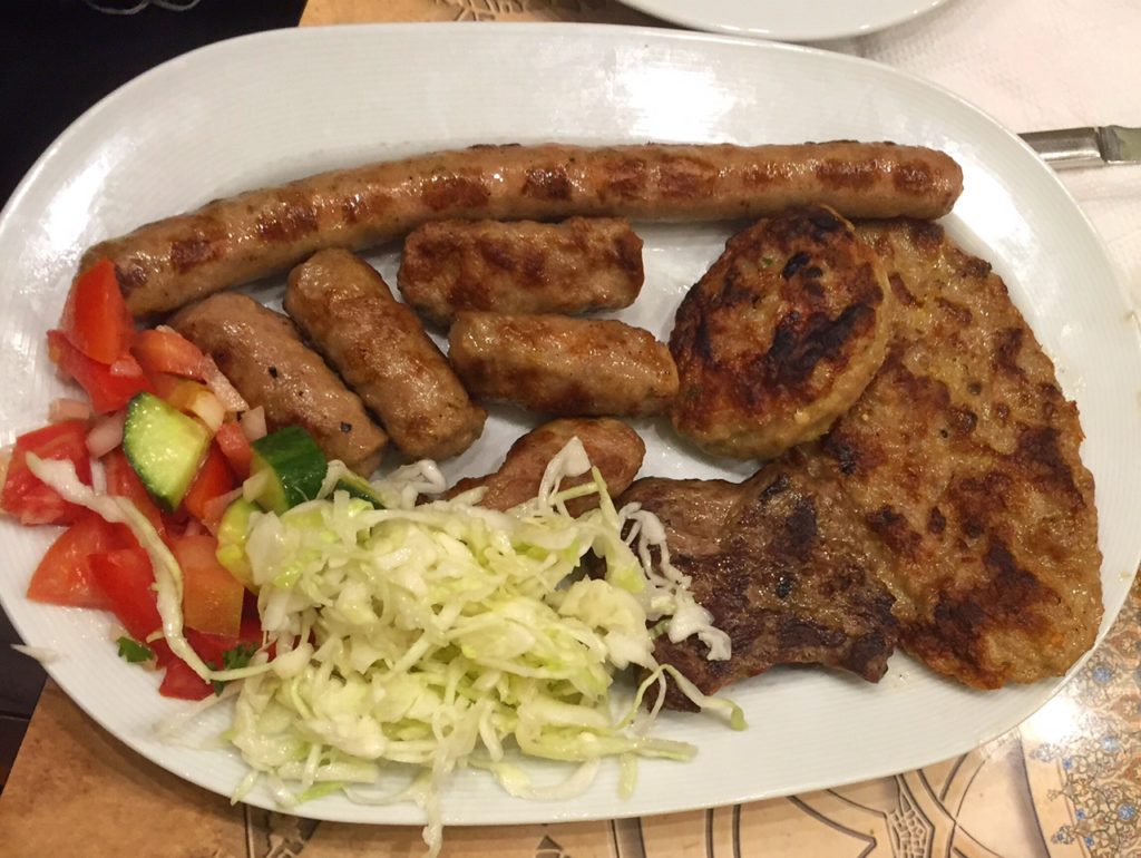 a giant plate of various grilled meats with tomato and cabbage