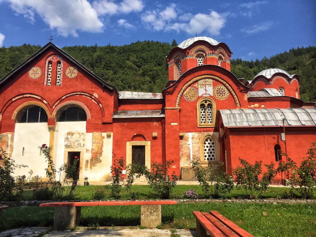 The gorgeous red monastery in Peja with forest behind it