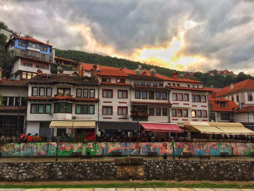 The cafes on the river banks of Prizren Kosovo with an explosively colorful sunset behind the houses