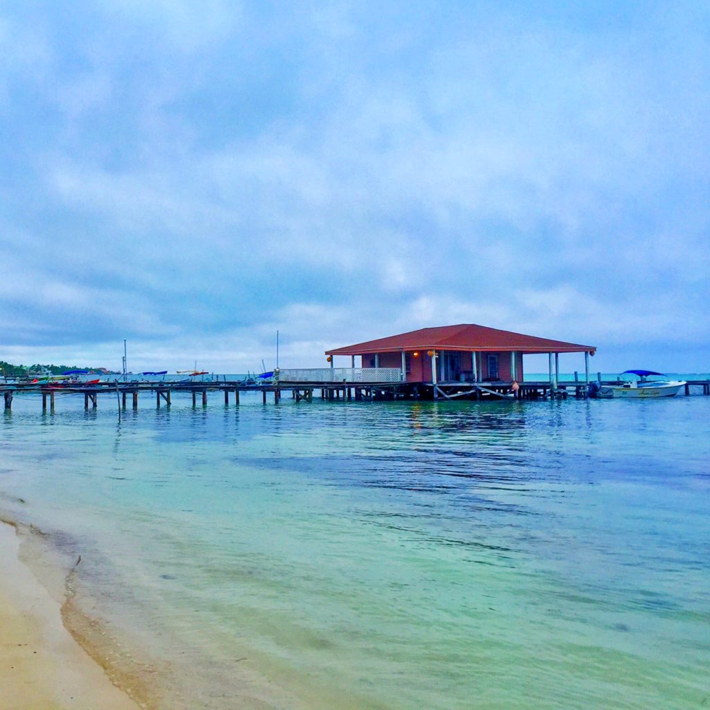 a red house built out on the dock with the beach and a boat