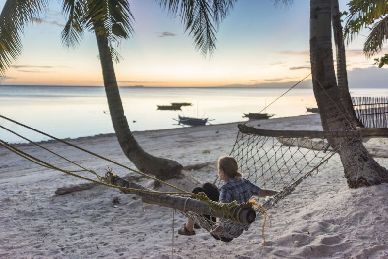 Margherita sitting in a hammock on the beach looking at the sunset with boats in the water