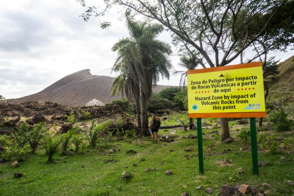 View of a smoking volcanic crater with text that says "hazard zone by impact of volcanic rocks from this point"