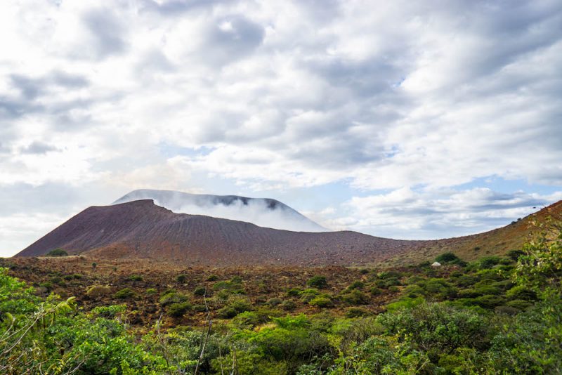 View of the smoking crater of Telica volcano with lots of gravel and greenery nearby