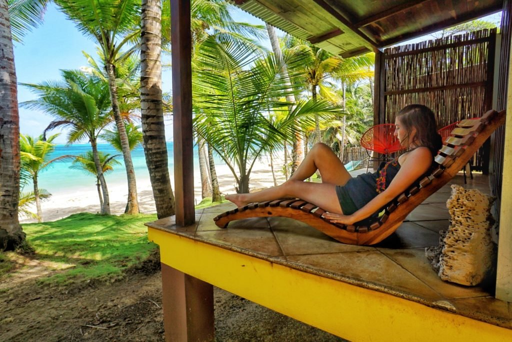 Allison Green sitting on a beach chair on a yellow cabana in the caribbean with palm trees and water around