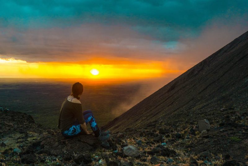 Allison wearing hiking clothes and sitting on the side of a crater of a volcano in Nicaragua, Telica volcano