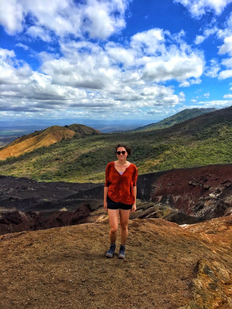 Allison wearing hiking boots, shorts, and a red shirt, hiking up a mountain in order to go volcano boarding, one of the more unique things to do in Nicaragua