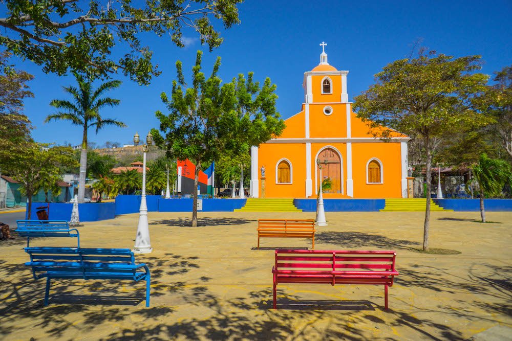 the orange and white church in san juan del sur with orange and blue benches