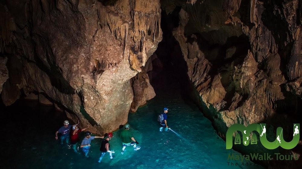 People walking through a cave system in Belize with flashlights and blue water