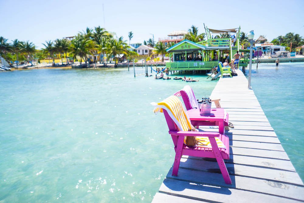 Beach chairs in pink with yellow towels on them and a green bar and some inner tubes and hammocks to relax on