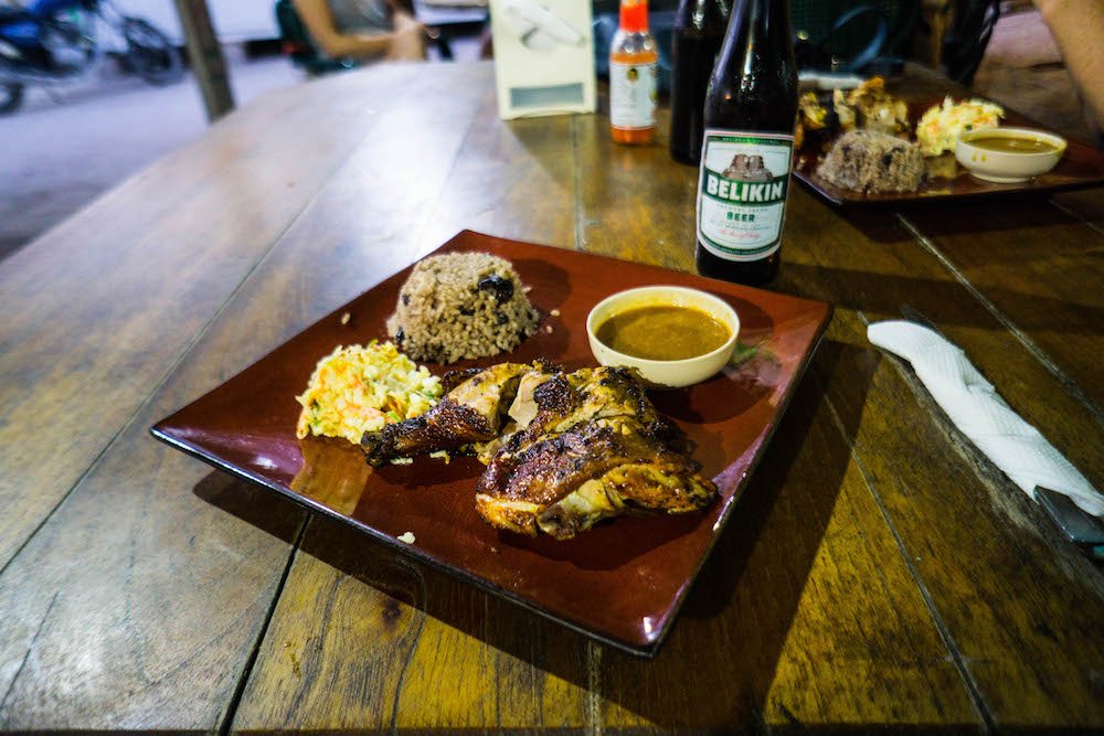 a plate of jerk chicken served with a belikin beer