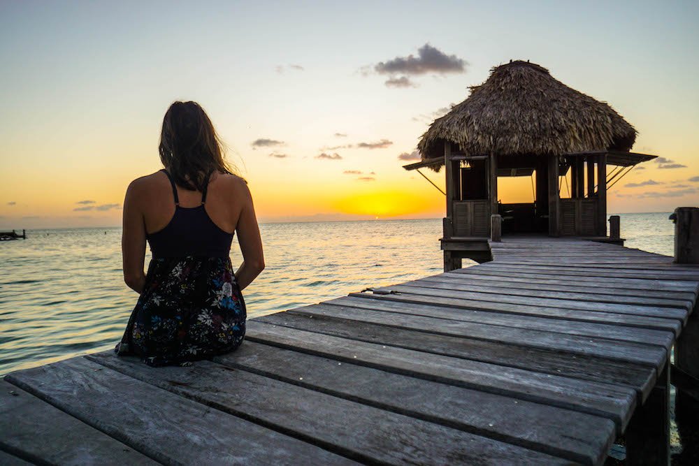 Allison Green in a dress sitting in front of the sunrise in Belize