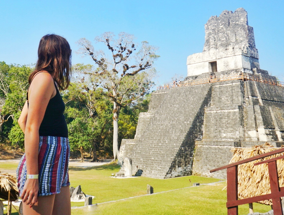 Allison wearing a black camisole and printed shorts,  looking at a pyramid in Tikal, Guatemala