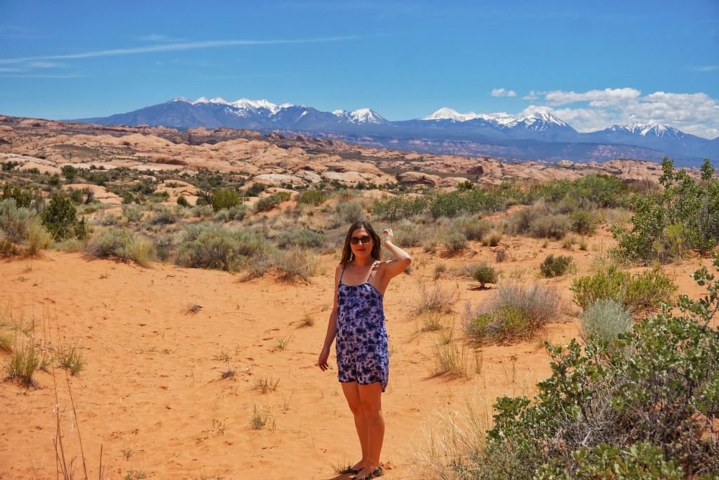 Allison standing in Arches National Park in moab, Utah with the mountains behind her