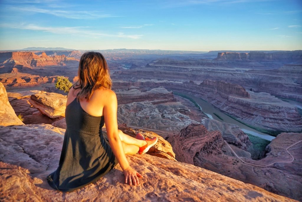 Sitting on the edge of Dead Horse Point State Park at sunset in a black dress looking out onto the river