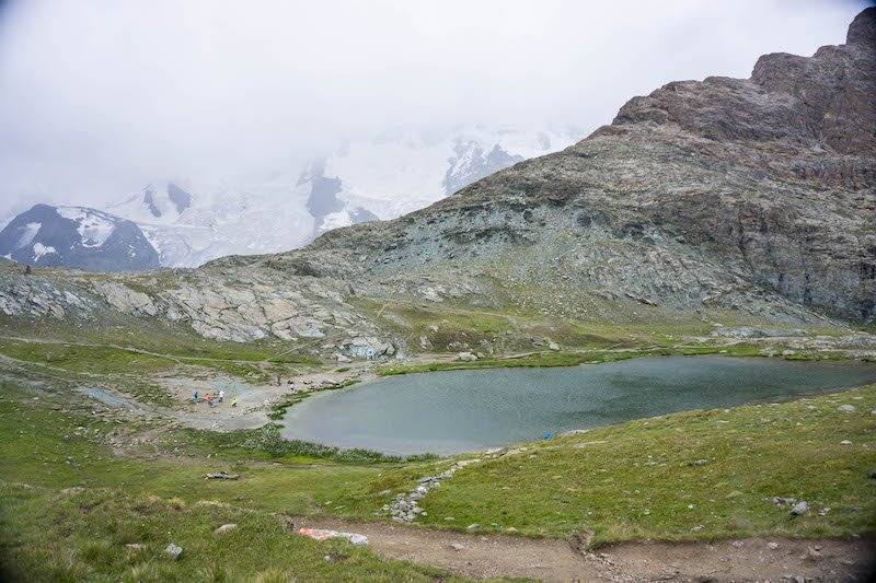 lake in the mountains of switzerland with a few people, clouds sweeping int he mountains