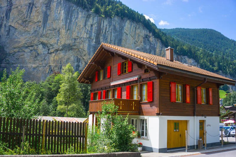 the charming town of lauterbrunnen with a wooden house with red window shutters and white ground level