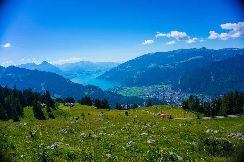 A beautiful scenery of the town of Interlaken seen from above, below, you can see a red train climbing up the railway.