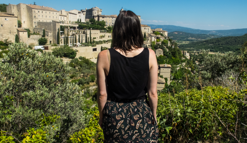 Allison Green, the article author, enjoying the views in Gordes in Provence, with sand-colored buildings and a hilltop view over the Provence area and Luberon valley