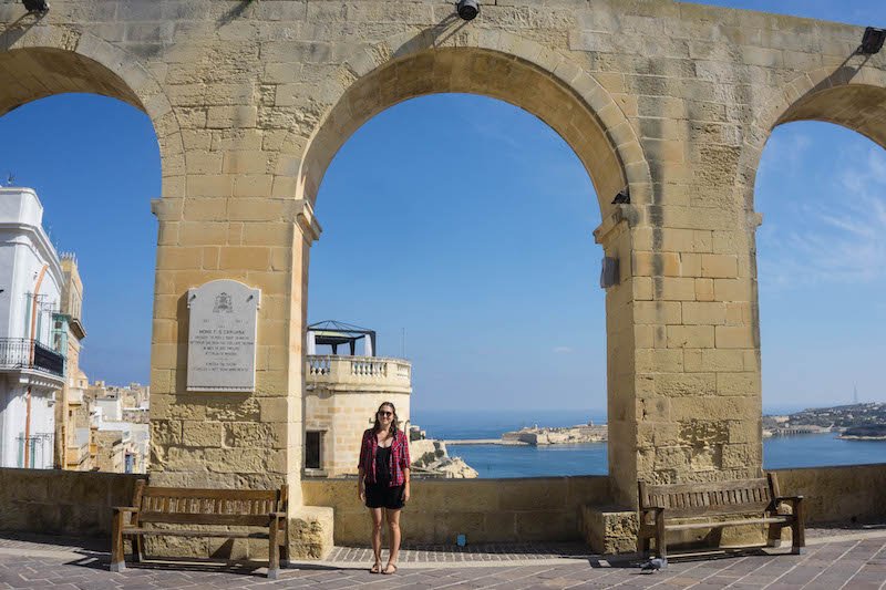 Allison standing in front of arches at the Upper Barrakka Gardens in Malta on a sunny day in October.