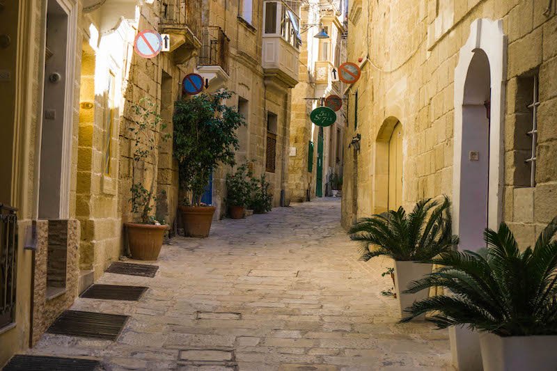 A sandstone-brick street in Malta's Birgu with colorful balconies and doorways