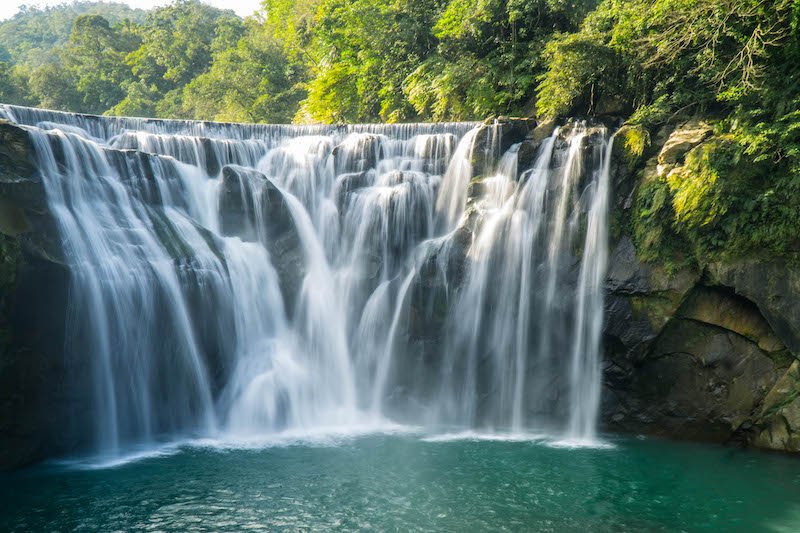 The gorgeous Shifen waterfall with cascading water falling into a blue pool surrounded by greenery