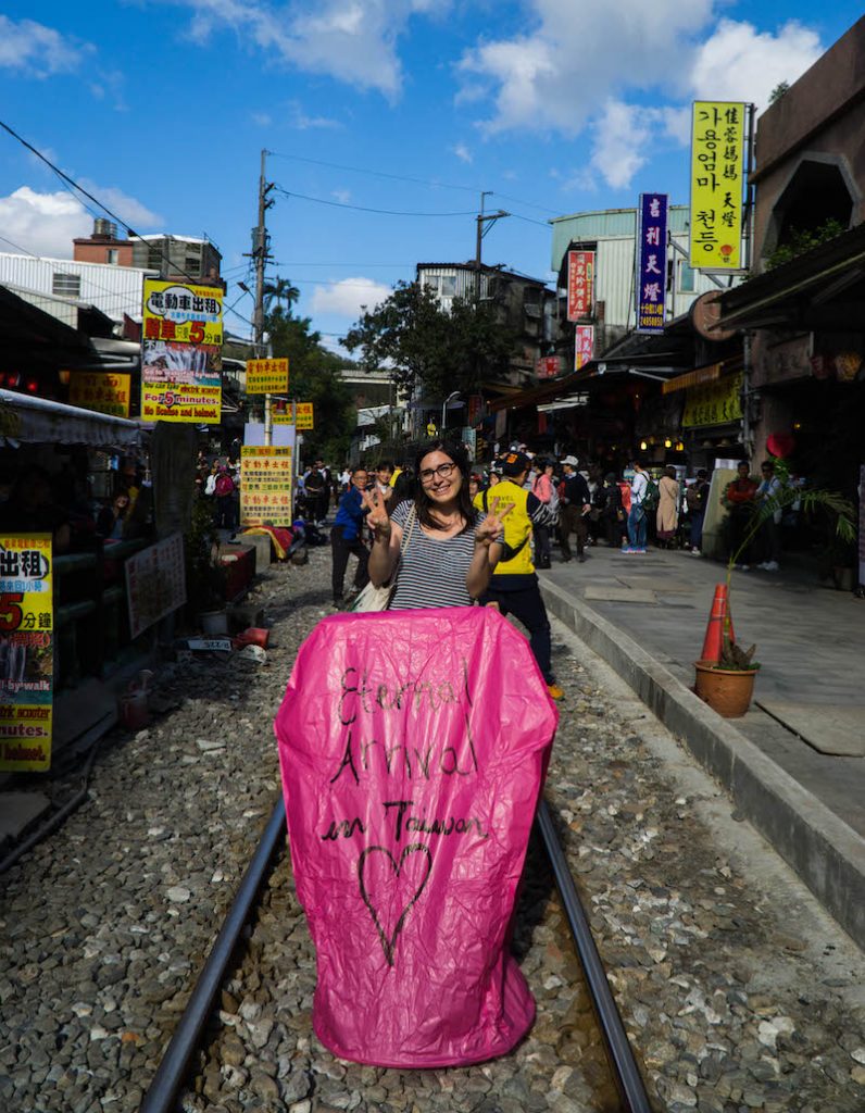 Allison Green standing with a pink balloon giving two peace signs with her hands and smiling