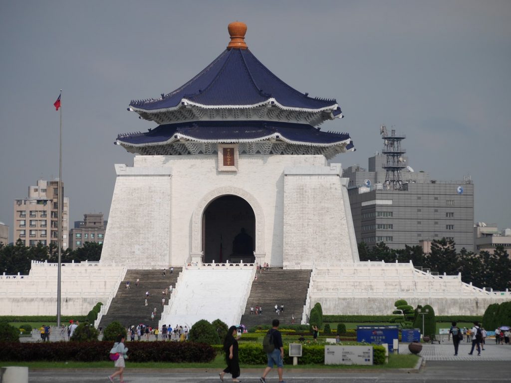 a white building with navy blue roof in downtown taipei with people walkinga round