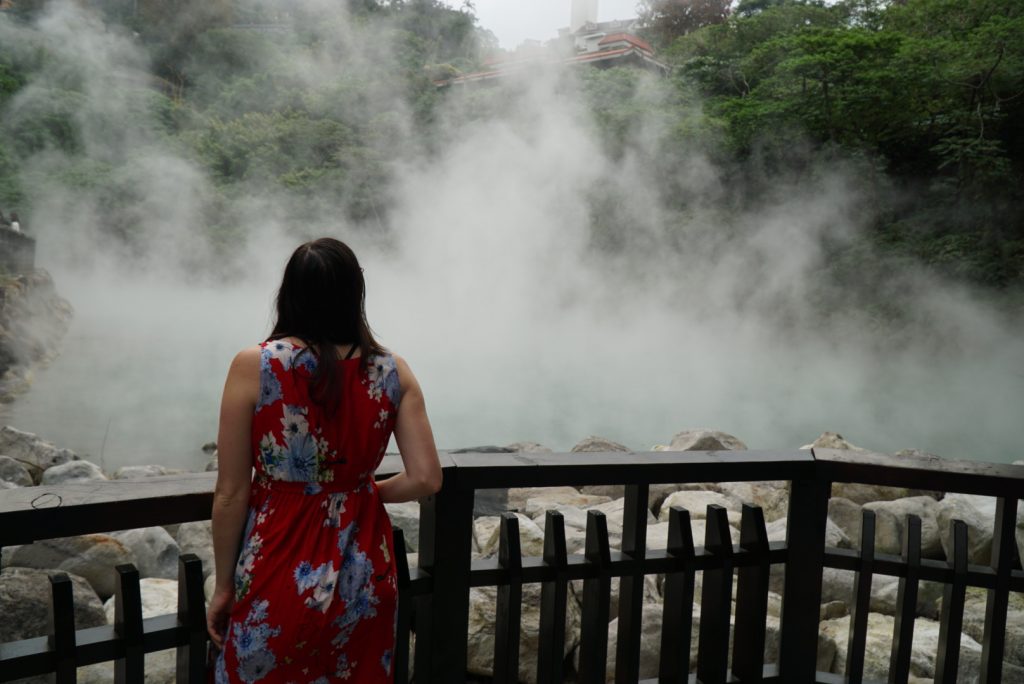 Allison Green standing before a hot spring that is billowing steam on a winter day