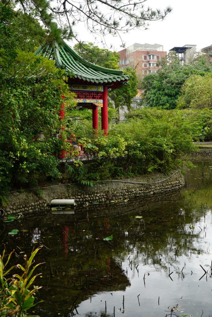 botanical garden in taipei with a red pagoda and buildings behind the garden.