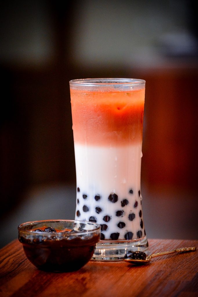 a tall glass of bubble tea with reddish color on top and tapioca pearls at the very bottom