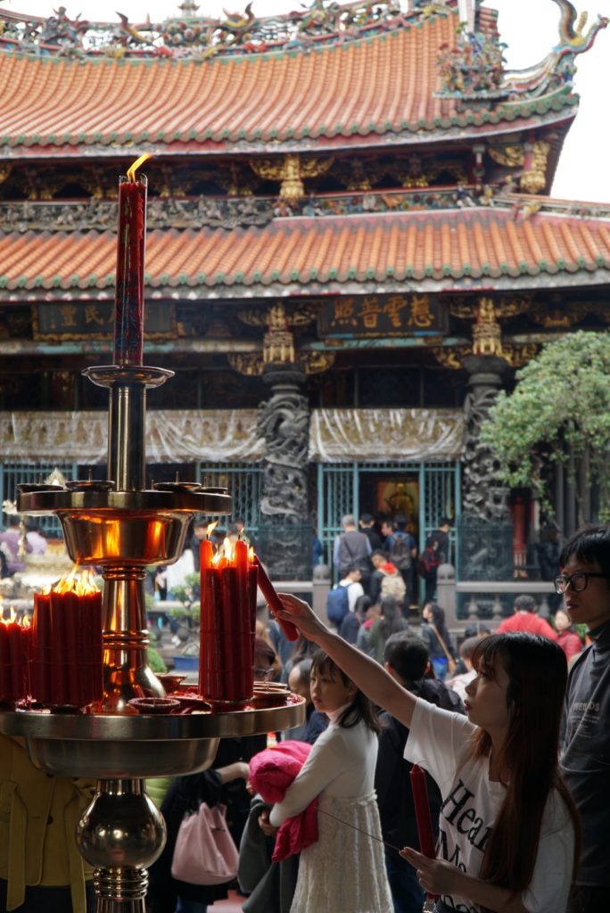 a woman lighting a candle at the busy longshan temple