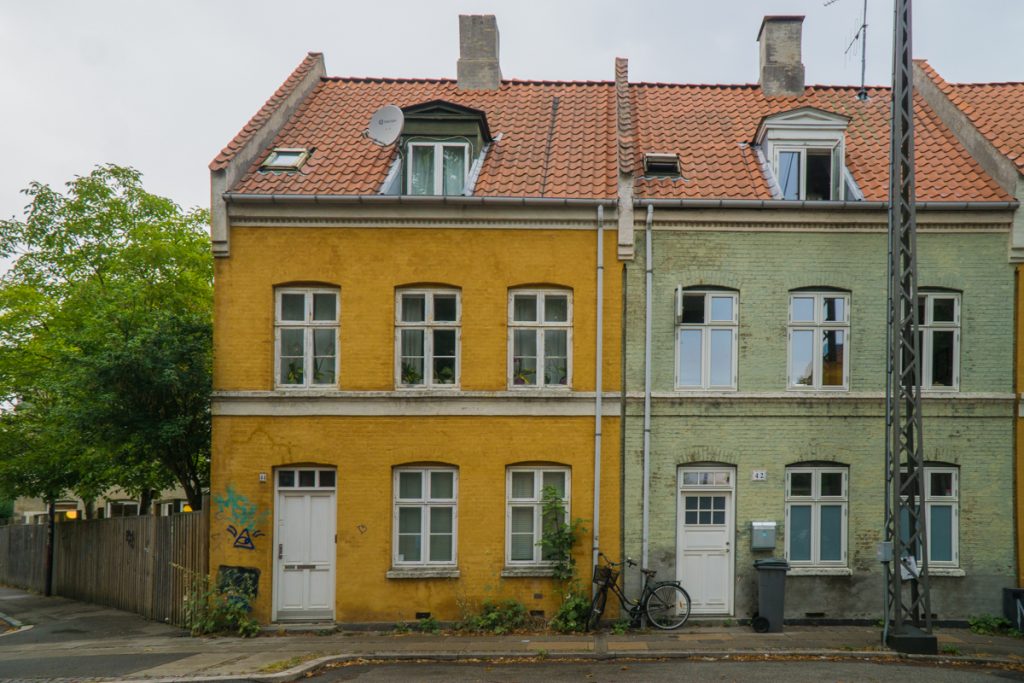 A winter house scene in Copenhagen with two beautiful buildings, yellow and green, and a bike