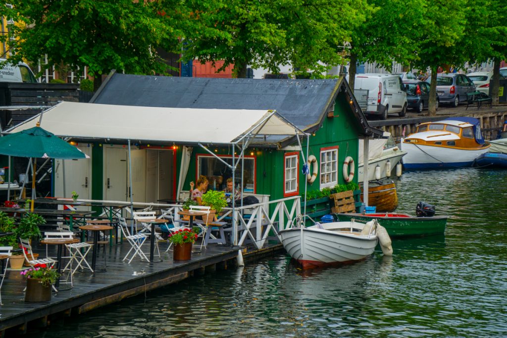 a green boathouse with a small white boat next to it and green trees