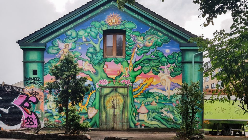 A colorful street art mural painting of a giant green dreamlike tree and faeries