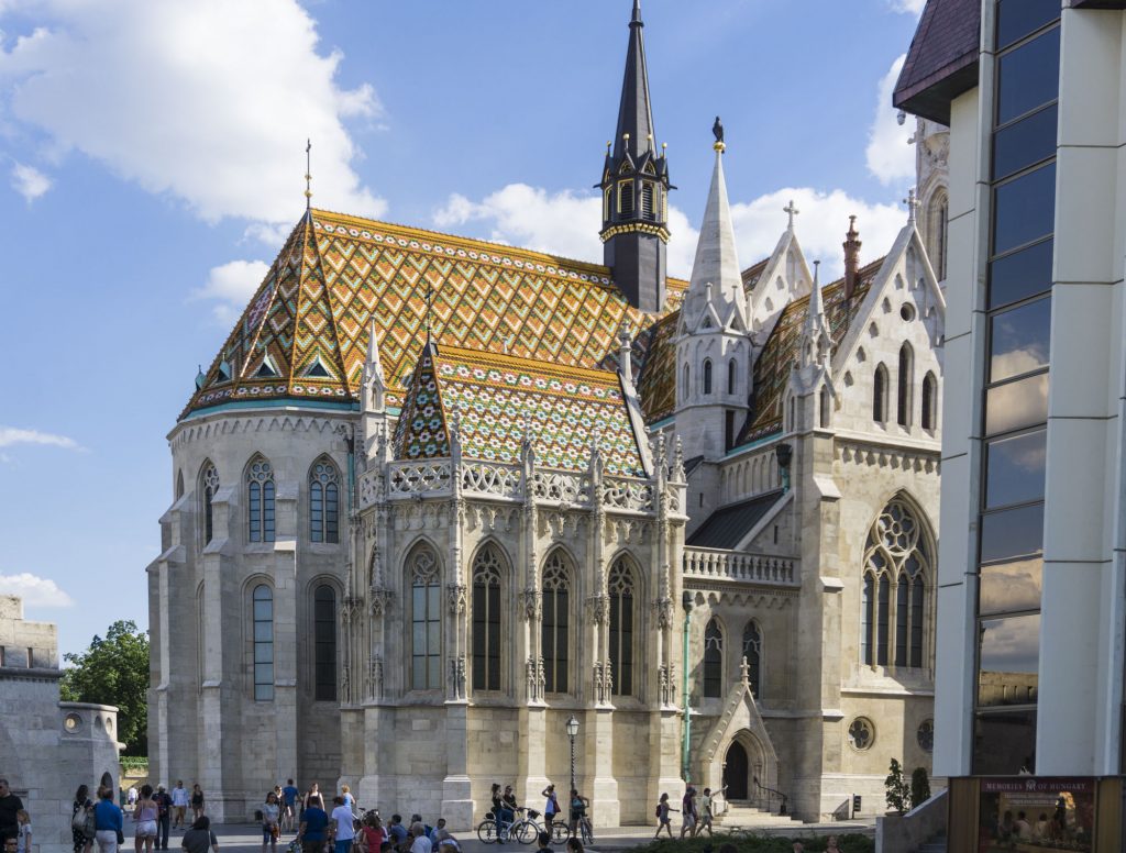 
View of a marble church with a brilliant multi-colored rooftop in yellow, orange, and green tile work on the rooftop, at the highest point of the city of Budapest