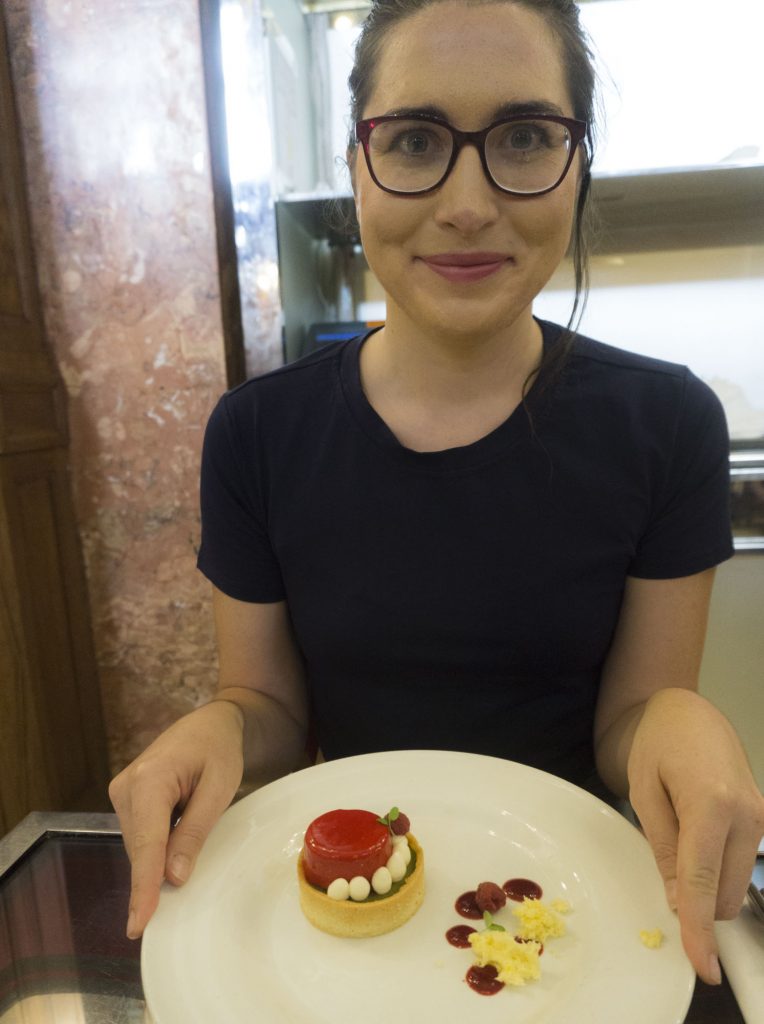 Allison Green wearing a blue shirt and glasses, smiling, holding the world's tiniest but very pretty cake