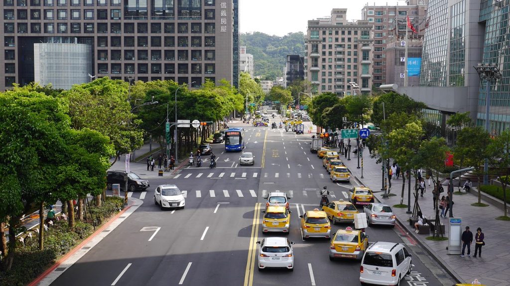 view of taxis and a busy taipei street with lots of people walking about during the daytime