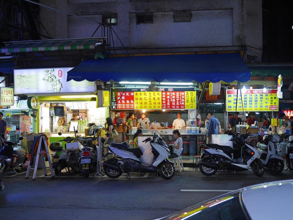 a taipei night market with chinese script writing and a few motorbikes and people eating at the markets