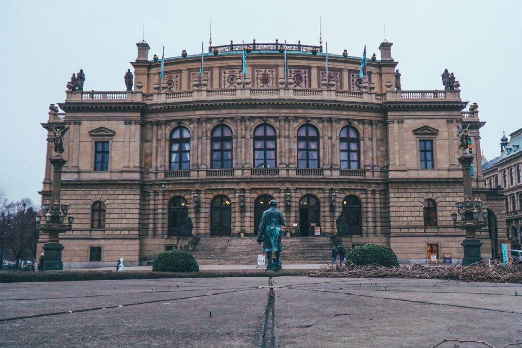 A dark overcast day showing one of Prague’s wonderful theaters with a statue in front of it