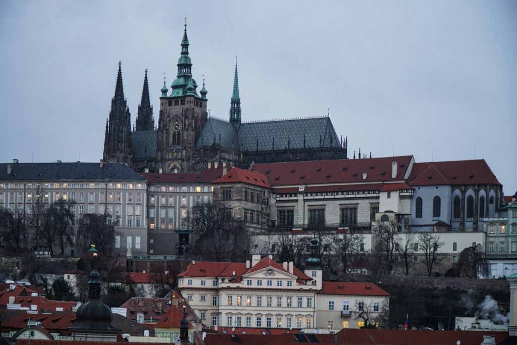 View from across the Vltava river as taken from Vysehrad castle, looking at the other castle of Prague, the main one in the castle district. The sky is dark and a few lights are just starting to come on in the city.