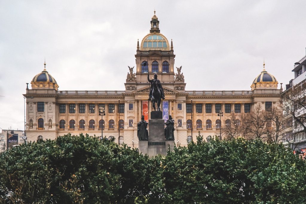 View of one of the most famous statues of a figure on a horse in Prague, which is standing in front of a classical architecture building that is part of the city’s architectural landscape.