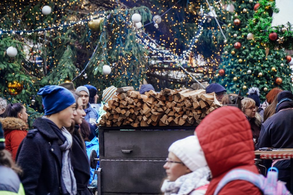 Several people in winter attire like winter jackets and hats while visiting a busy Prague Christmas market during December in the city