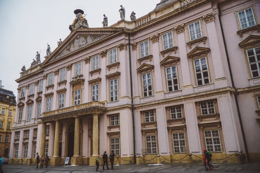 A light pink building with pillars and a small crowd in front of it in the Bratislava city center.