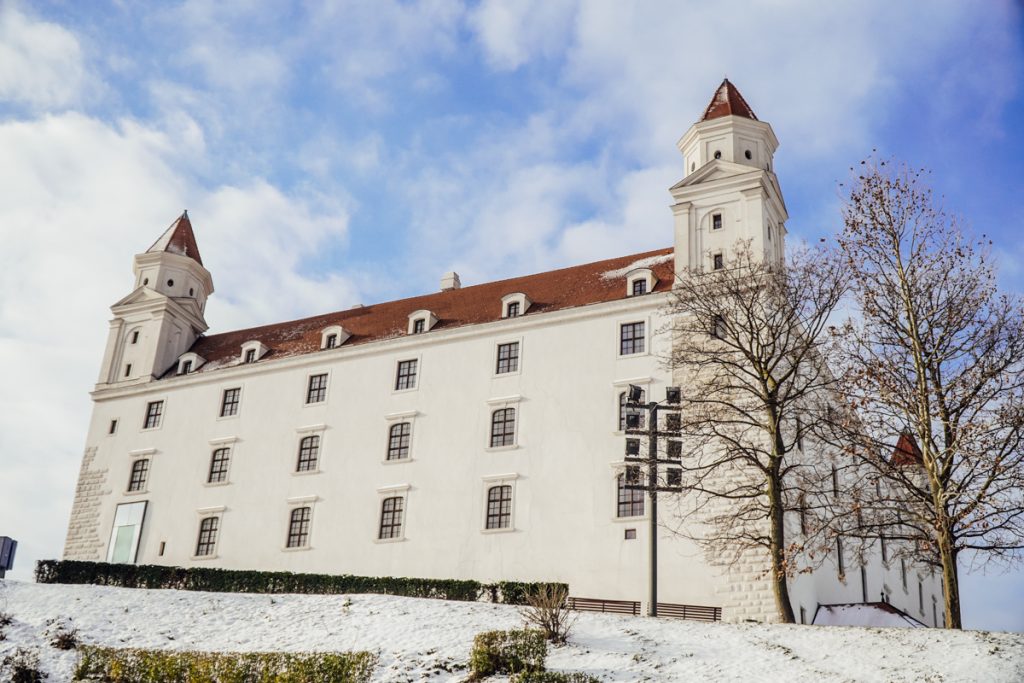 White castle building with red roof covered in snow and with a partly cloudy sky behind it.