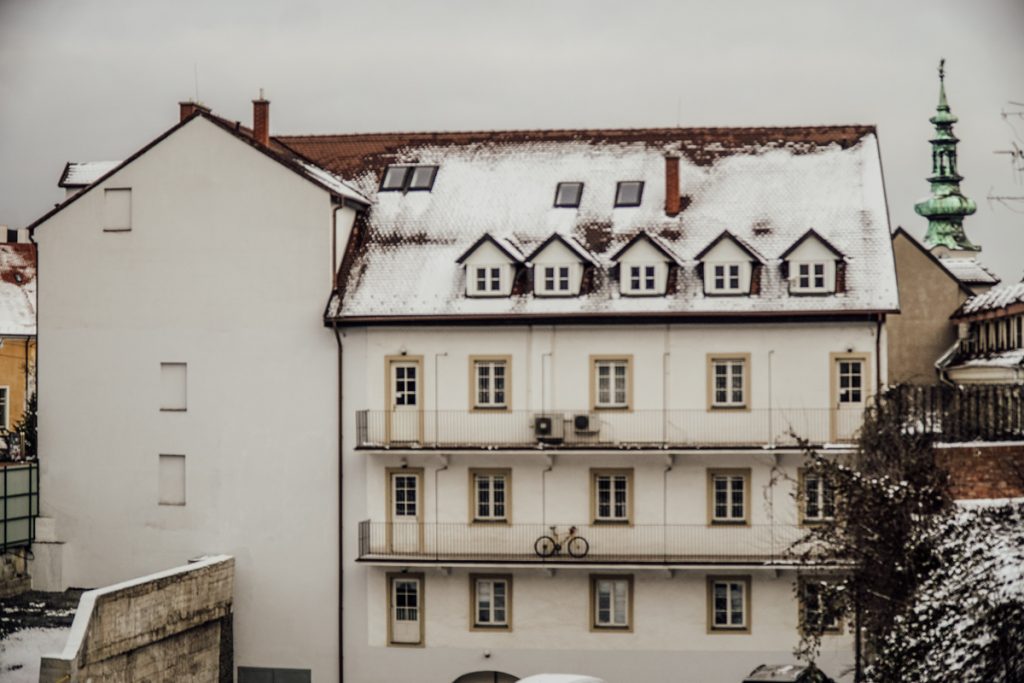Snow covered white building in Bratislava as seen in the winter period with trees and skyline visible behind it.