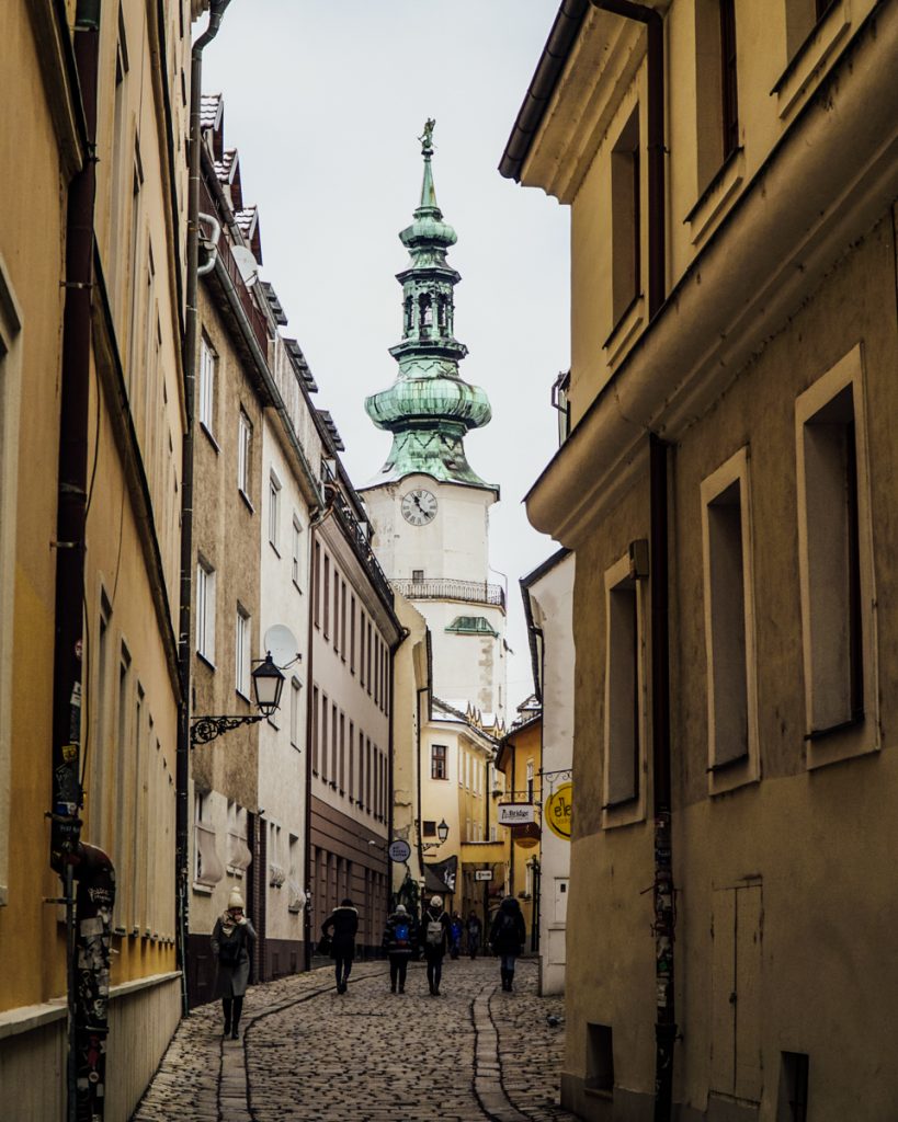 Another street scene in Bratislava with a large church and tower visible at the end of the alleyway or small street.